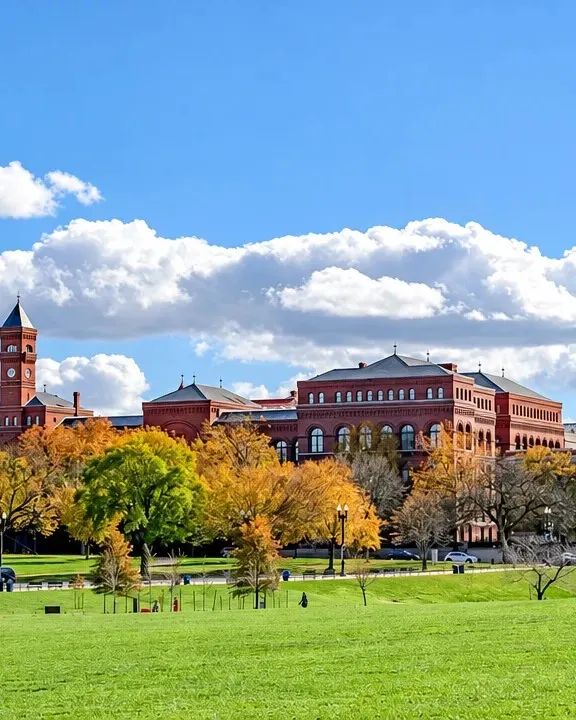 Red-brick university buildings across a wide green lawn on a sunny autumn day
